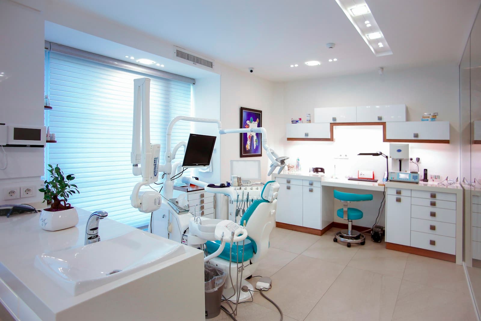 A bright, modern dental treatment room with a teal chair and white cabinetry