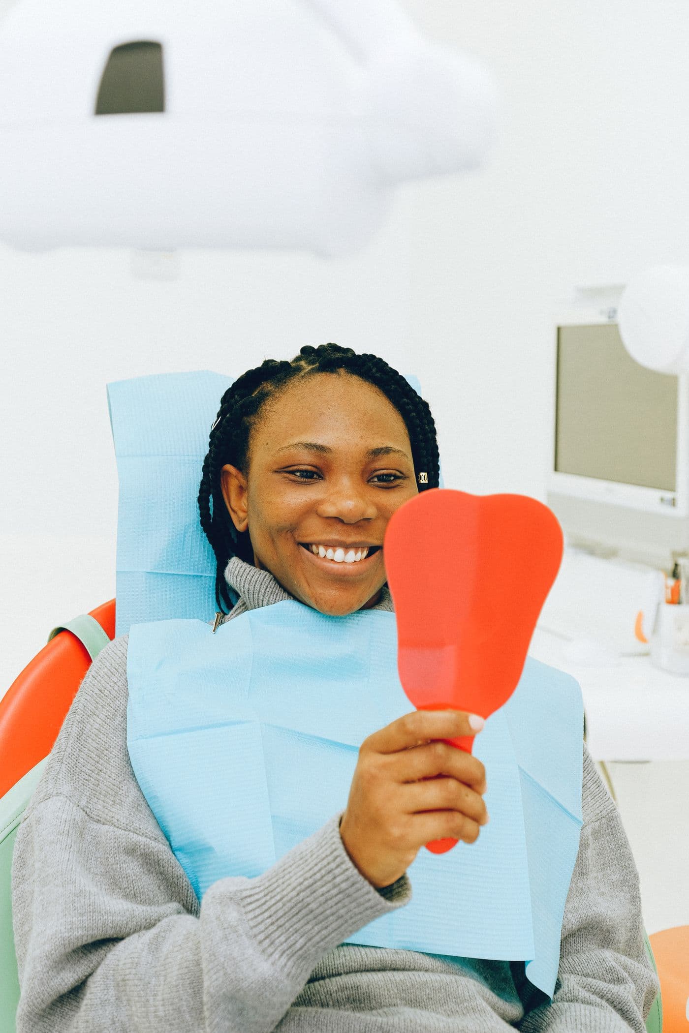 A patient smiling while looking at her teeth in a hand mirror